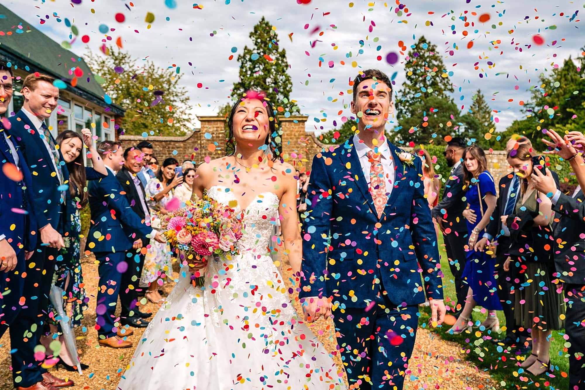 Surrey Wedding Photography, wedding couple walking through a cloud of confetti made up of circular coloured paper discs captured at Frensham Hall wedding